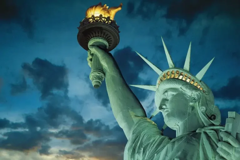 Close-up of the Statue of Liberty holding the torch against a dramatic evening sky in New York Harbor